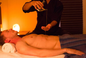 A picture of Rei, the Japanese male massage therapist giving an oil massage to a male client.