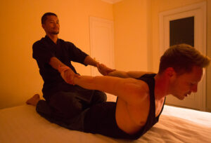 A picture of Rei, the Japanese male massage therapist giving a traditional thai massage to a male client.